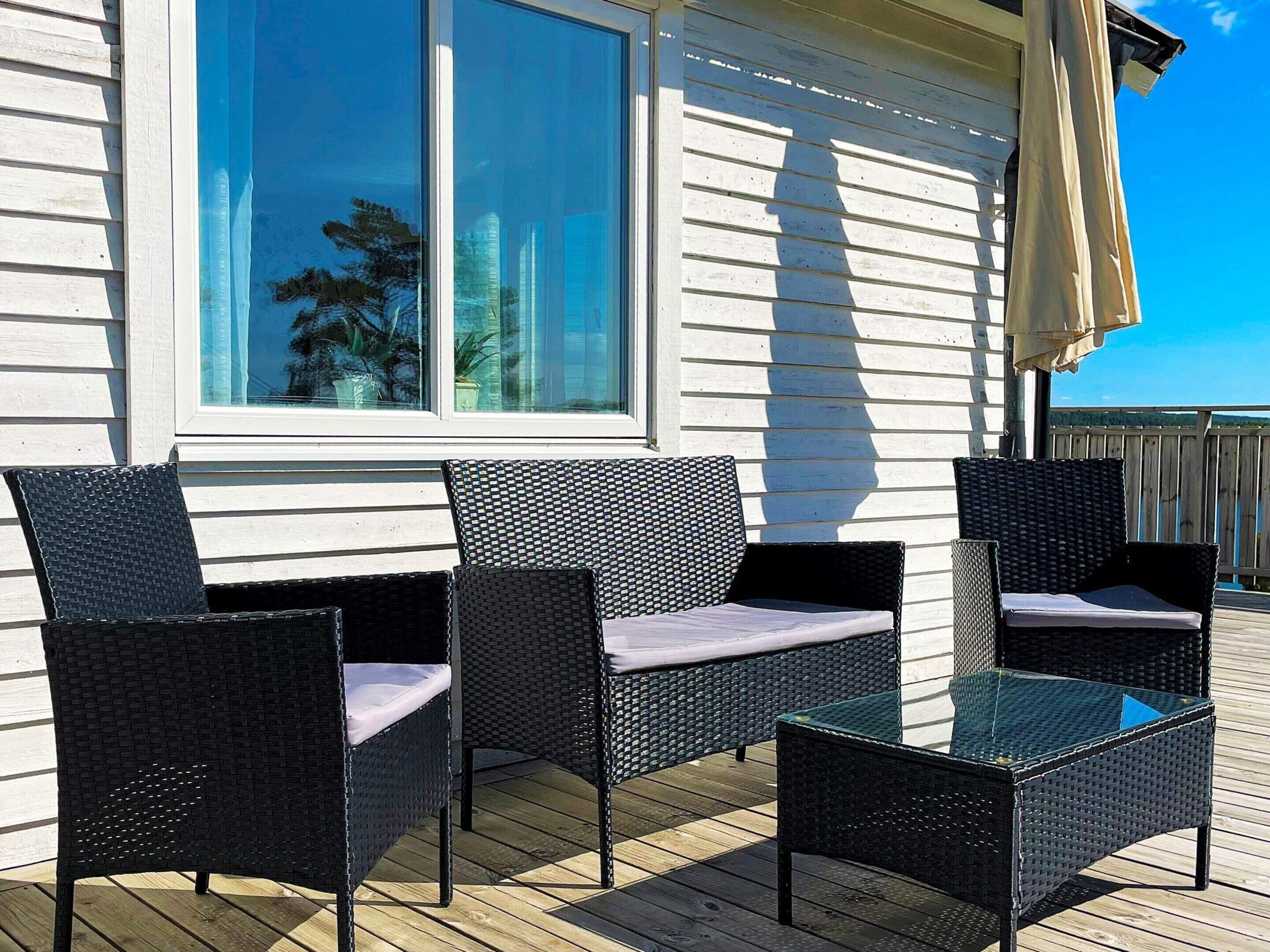 A deck with wicker furniture and a glass table, overlooking a white building with windows.