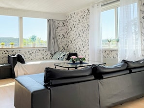 A modern living room with a sofa, a glass coffee table, and a view of the outdoors through large windows.