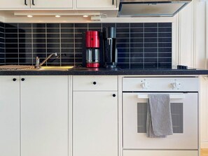 A kitchen with white cabinets, a black countertop, a red coffee maker, and a stainless steel oven. - 4 Star Holiday Home in Uddevalla (Uddevalla)