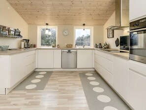 A modern kitchen with white cabinetry, a dishwasher, a clock, and a large window.