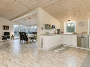 A modern kitchen with white cabinetry, a dining area with a wooden table and chairs, and a large window providing natural light.