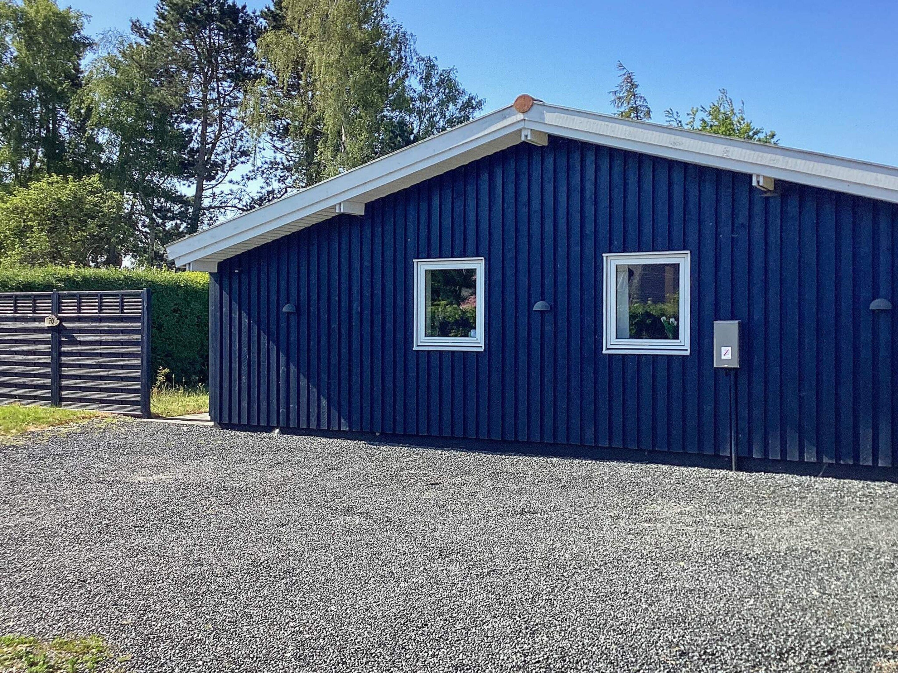 A blue building with two windows and a gravel driveway.