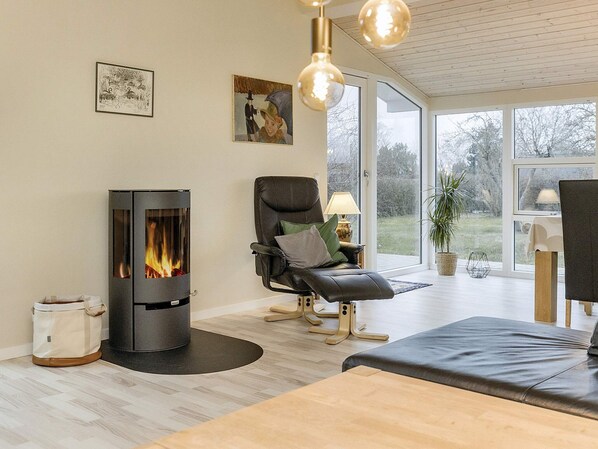 A modern living room with a wood-burning stove, a leather chair, and a large window offering a view of the outdoors.