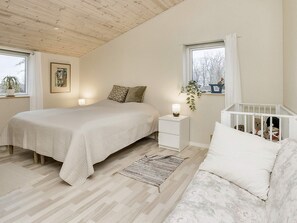 A bedroom with a bed, bedside table, nightstand, crib, and a window with a view.