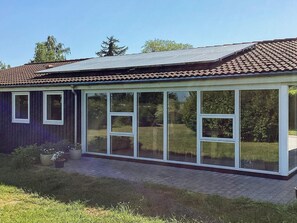 Et hus med tegltag, et glashus og en murstenssti, der fører til indgangen.
