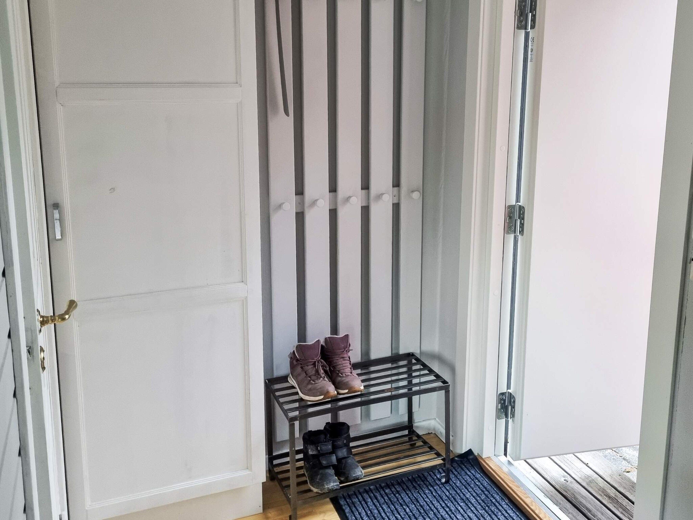 Un couloir avec un porte-chaussures contenant des bottes et des baskets, une porte dotée d’une poignée en laiton et un plancher en bois.