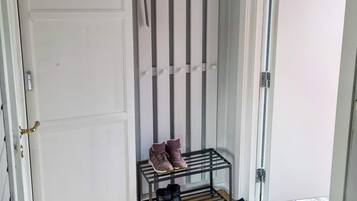 Un couloir avec un porte-chaussures contenant des bottes et des baskets, une porte dotée d’une poignée en laiton et un plancher en bois.