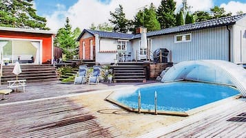 A residential area with a swimming pool, a wooden deck, and a house with a red door.