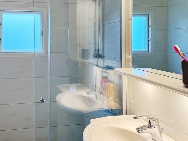 A bathroom with a glass-enclosed shower, a sink, and a mirror.