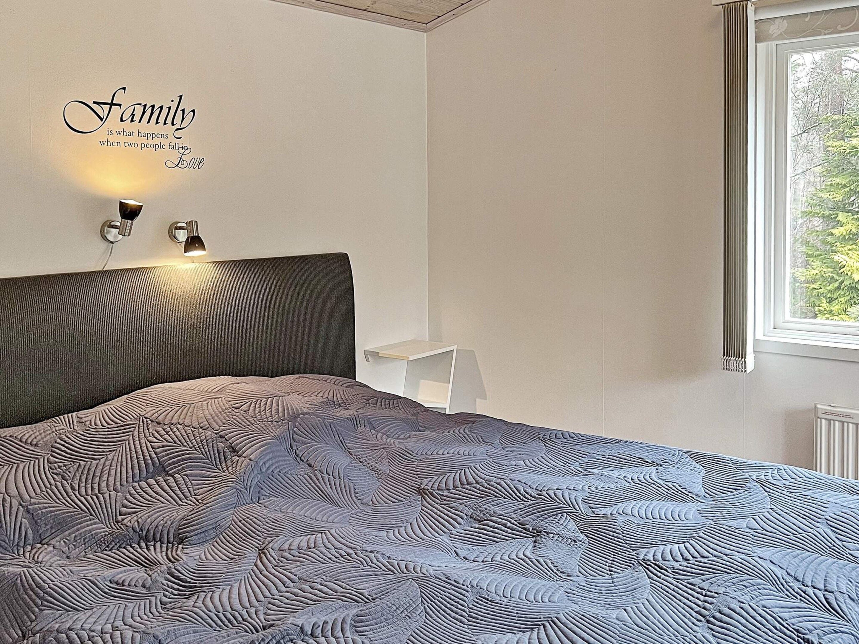 A bedroom with a bed, a wall-mounted light, and a window.