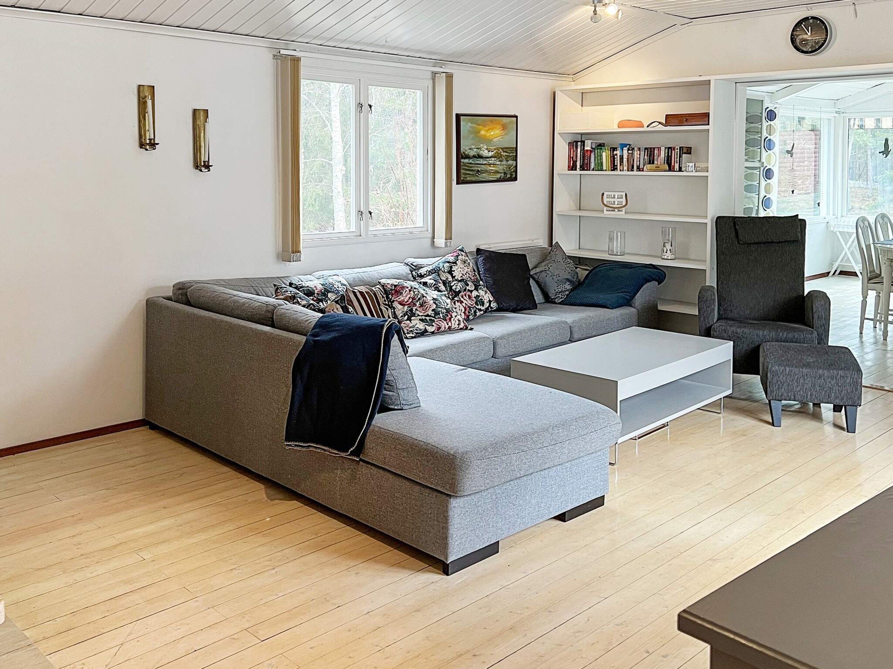 Ein modernes Wohnzimmer mit einem grauen Ecksofa, einem Couchtisch, einem Bücherregal und einem Essbereich mit Tisch und Stühlen.