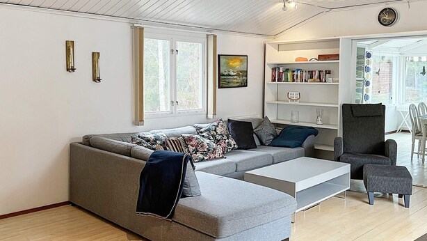 A modern living room with a grey sectional sofa, a coffee table, a bookshelf, and a dining area with a table and chairs. - 5 Star Holiday Home in Nynashamn (Nynashamn)