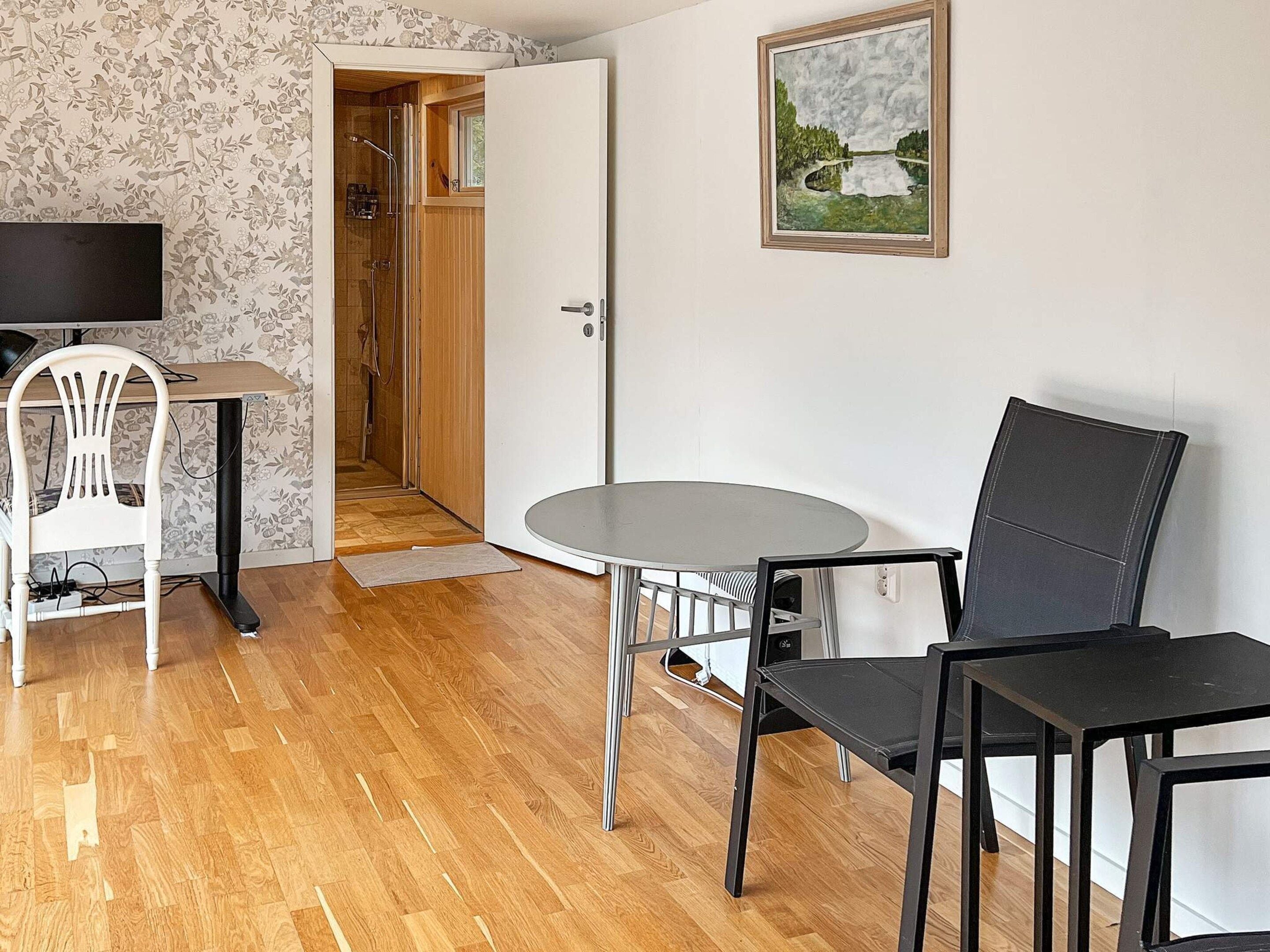 Une pièce avec un plancher en bois, une table ronde, deux chaises, un téléviseur, une porte donnant sur une douche et un tableau encadré accroché au mur.