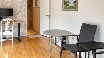 Une pièce avec un plancher en bois, une table ronde, deux chaises, un téléviseur, une porte donnant sur une douche et un tableau encadré accroché au mur.