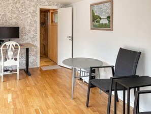 A room with a wooden floor, a round table, two chairs, a television, a door leading to a shower, and a framed painting on the wall. - 5 Star Holiday Home in Nynashamn (Nynashamn)