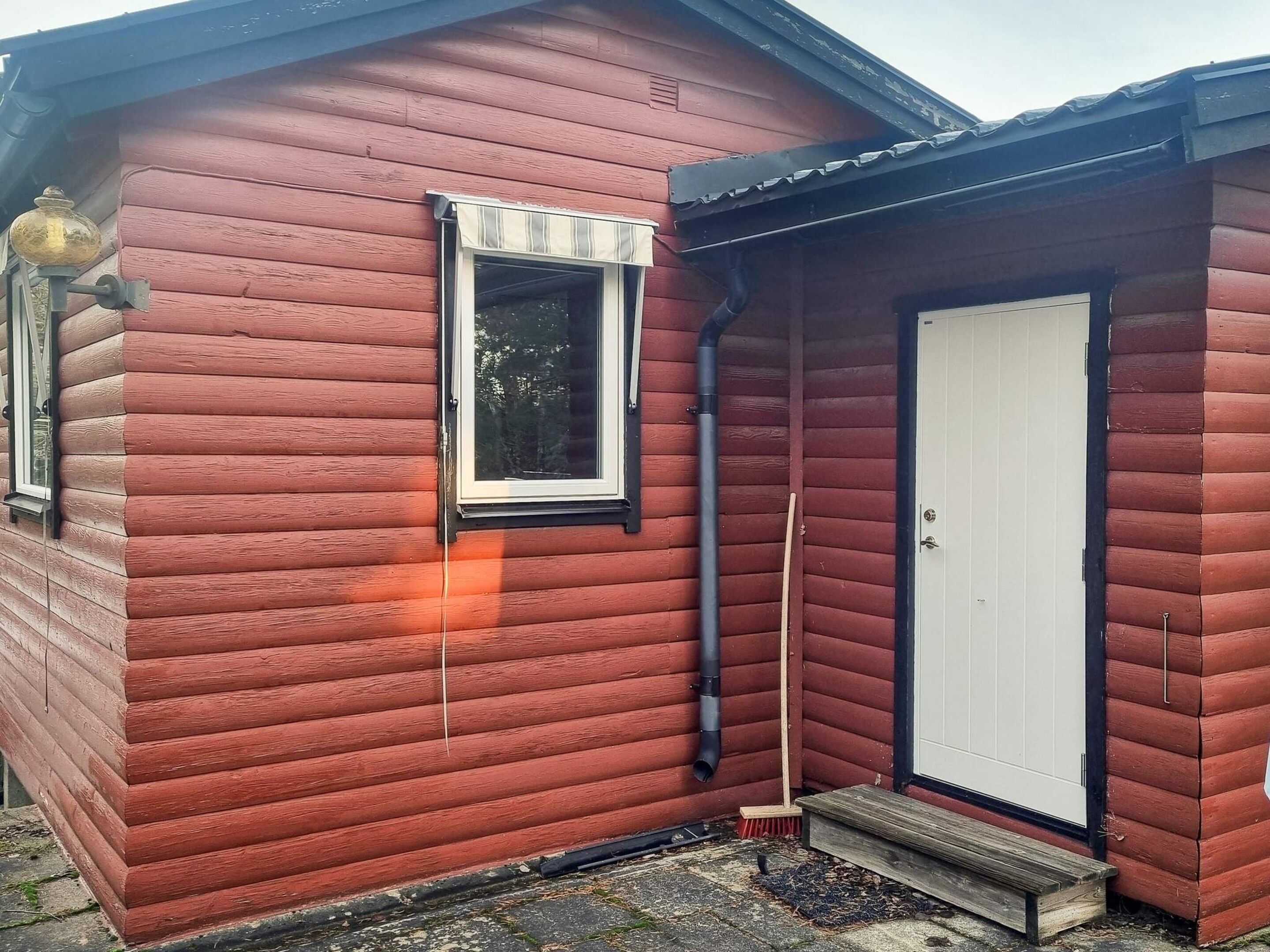 En liten, envåningsbyggnad av trä med en vit dörr och ett fönster med svart ram.