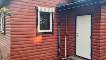 A small, single-story wooden building with a white door and a window with a black frame.