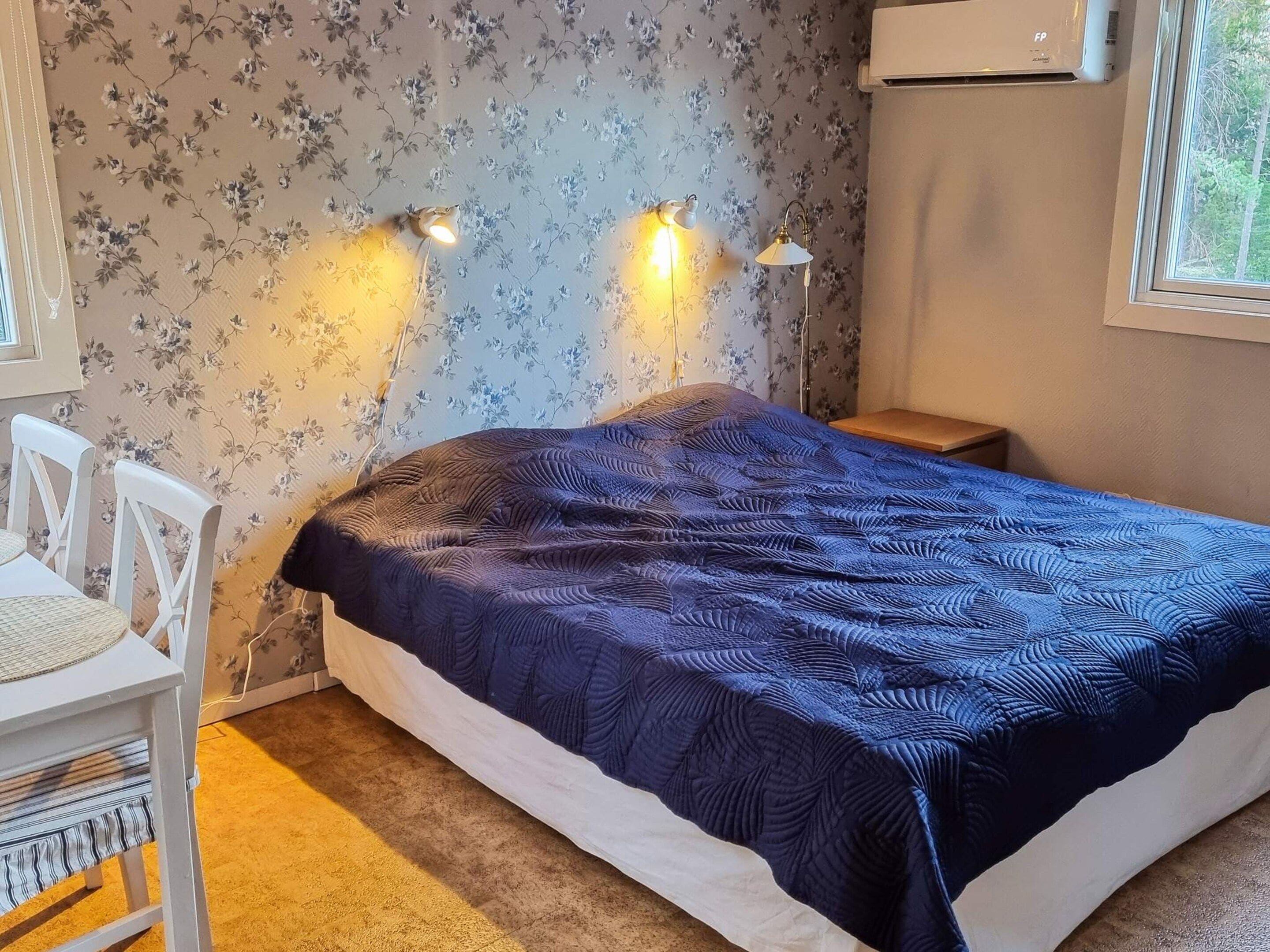 Quarto com cama, duas luminárias na parede, uma cadeira e uma janela.