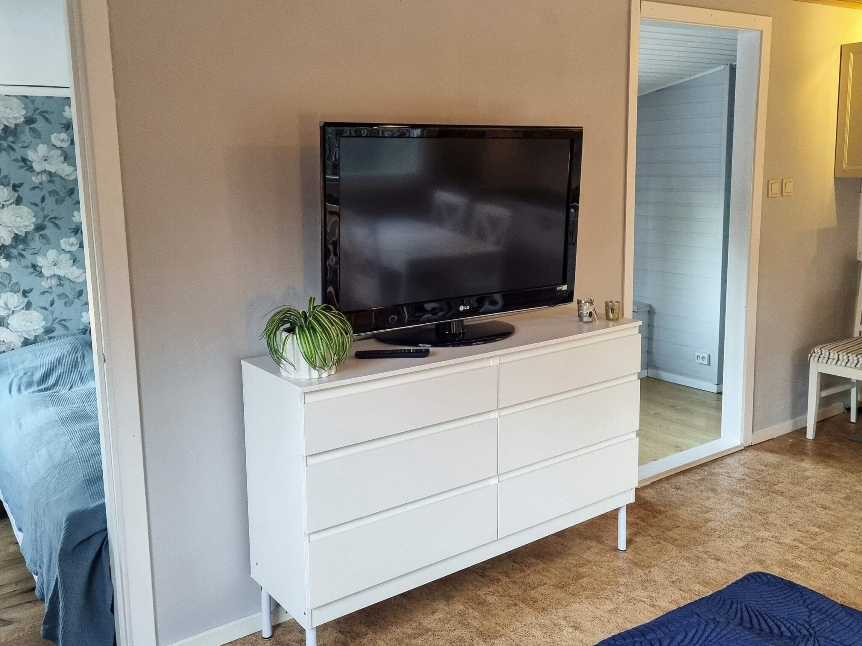 Una televisione a schermo piatto su una cassettiera bianca in una stanza con pavimento in legno.