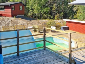 A pool area with a wooden deck, a red building, and a forested background. - 5 Star Holiday Home in Nynashamn (Nynashamn)