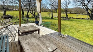 An outdoor wooden deck with a table and benches, surrounded by a grassy field and trees. - 5 Person Holiday Home in Brosarp (Brosarp)
