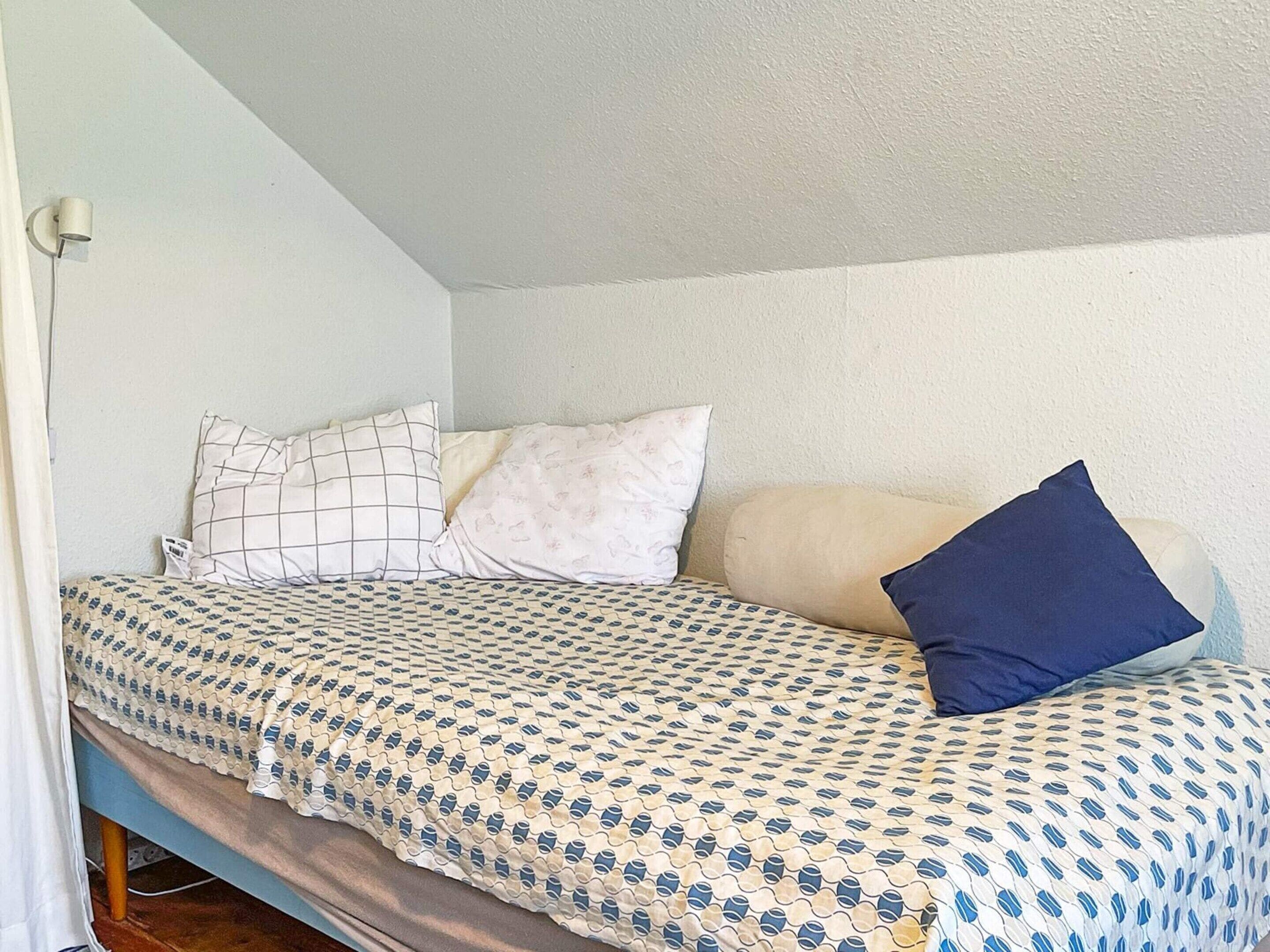 Un lit simple avec une literie à motifs, une lampe fixée au mur et une fenêtre donnant sur un paysage agréable.