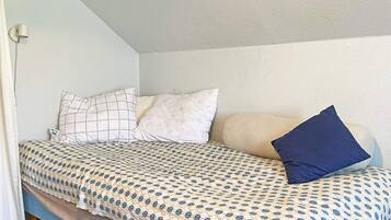 Una cama individual con ropa de cama estampada, una lámpara de pared y una ventana con vistas.