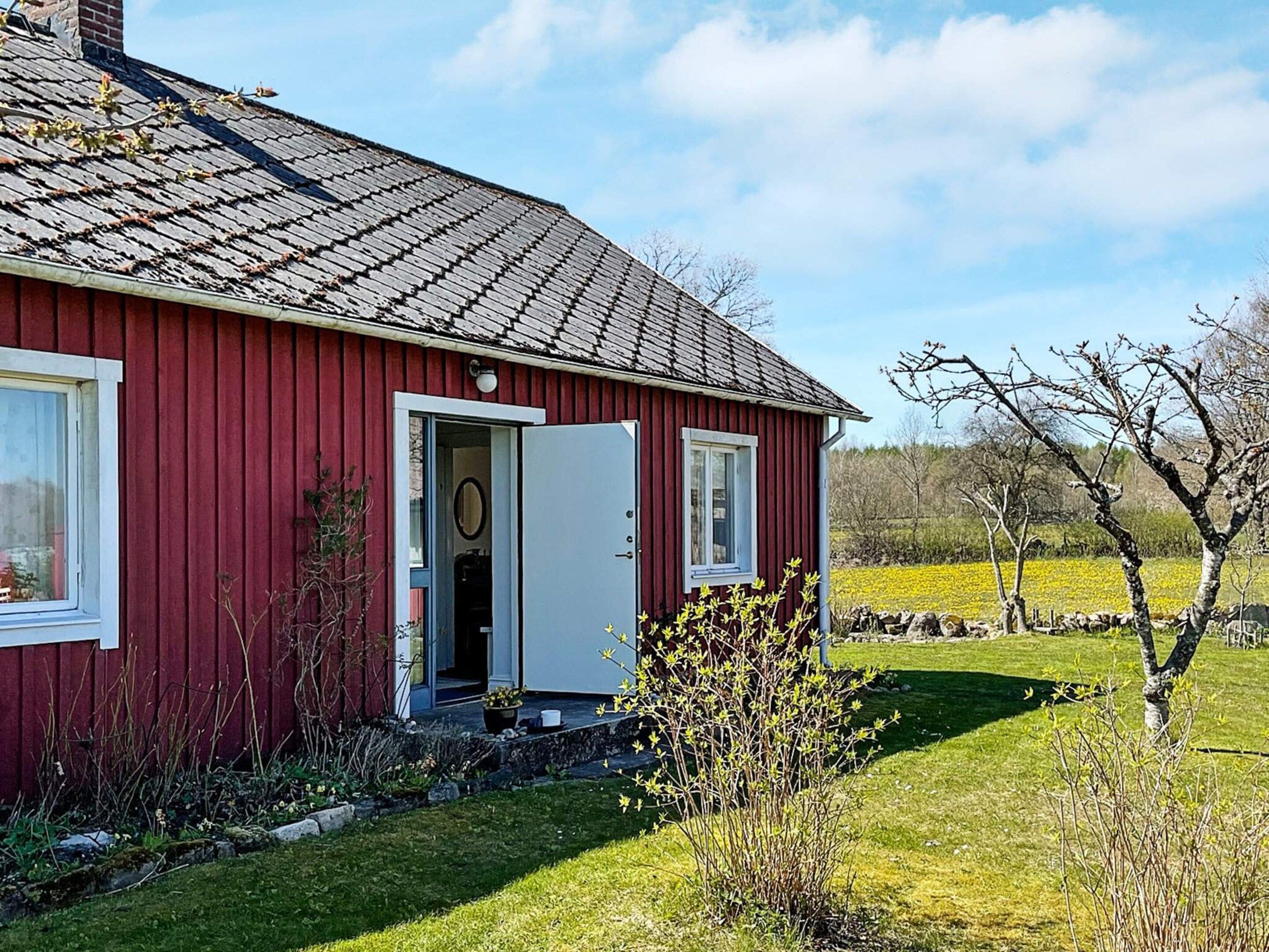 Una casa de madera roja con puerta blanca, un pequeño porche y un jardín con césped y arbustos.