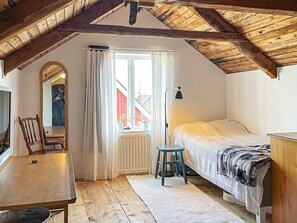 Un dormitorio con techo de madera, una cama, un escritorio, una silla y una ventana con cortinas.