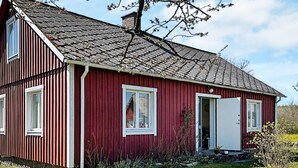 A red wooden house with a sloped roof, a chimney, and a small porch with a door. - 5 Person Holiday Home in Brosarp (Brosarp)