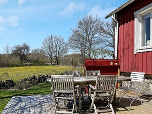 An outdoor patio with a wooden table and chairs, a red building with a window, and a field of yellow flowers in the background. - 5 Person Holiday Home in Brosarp (Brosarp)