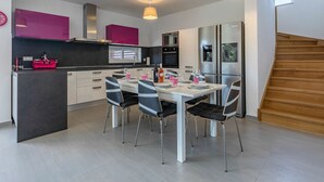 Una cocina moderna con comedor, que cuenta con una isla central, electrodomésticos de acero inoxidable e iluminación colgante.