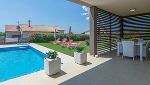 Zona de piscina exterior moderna con vista despejada a una casa al fondo.