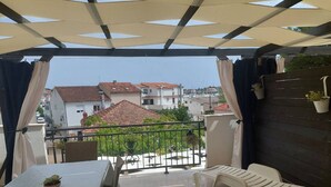 A covered outdoor area with a table and chairs, a view of buildings in the background, and a railing. - Apartments Paula - One Bedroom Apartment With Terrace 1 (Tisno)