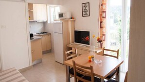 A compact kitchen with a refrigerator, microwave, and stove. There's a dining table with chairs and a TV on a stand. - Apartments Paula - One Bedroom Apartment With Terrace 1 (Tisno)
