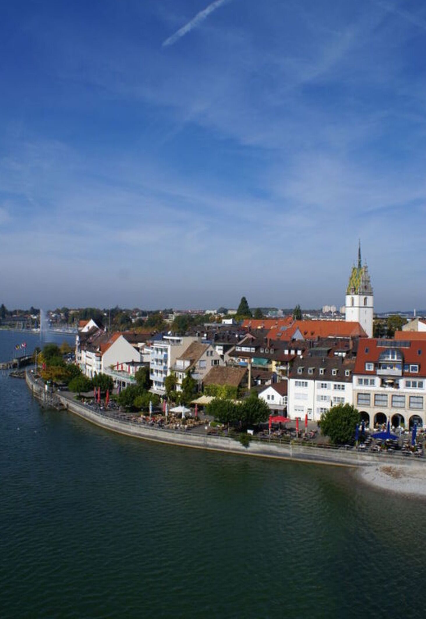 A riverside town with historic buildings, a prominent church tower, and a waterfront promenade.