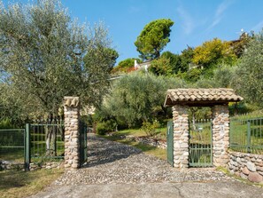 A stone gate leading to a property surrounded by olive trees and a large tree in the background. - Spacious Holiday Home in Marciaga With Garden (Costermano sul Garda)