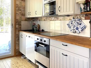 A kitchen with a wooden countertop, white cabinets, a stainless steel oven, and a window with a view of trees. - 4 Person Holiday Home in Gusum (Valdemarsvik)