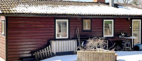 A wooden cabin with a tiled roof, a wooden deck, and a small shed.