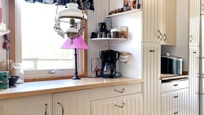Une cuisine avec des meubles blancs, une machine à café et une fenêtre avec une lampe.