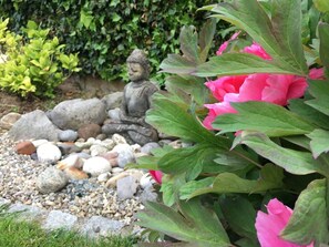 Un jardín con una estatua de Buda, peonías y diversas rocas.