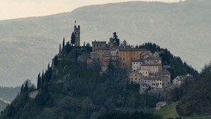 Une ville historique perchée sur une colline, avec un clocher d’église imposant, entourée d’une végétation luxuriante et de bâtiments traditionnels.