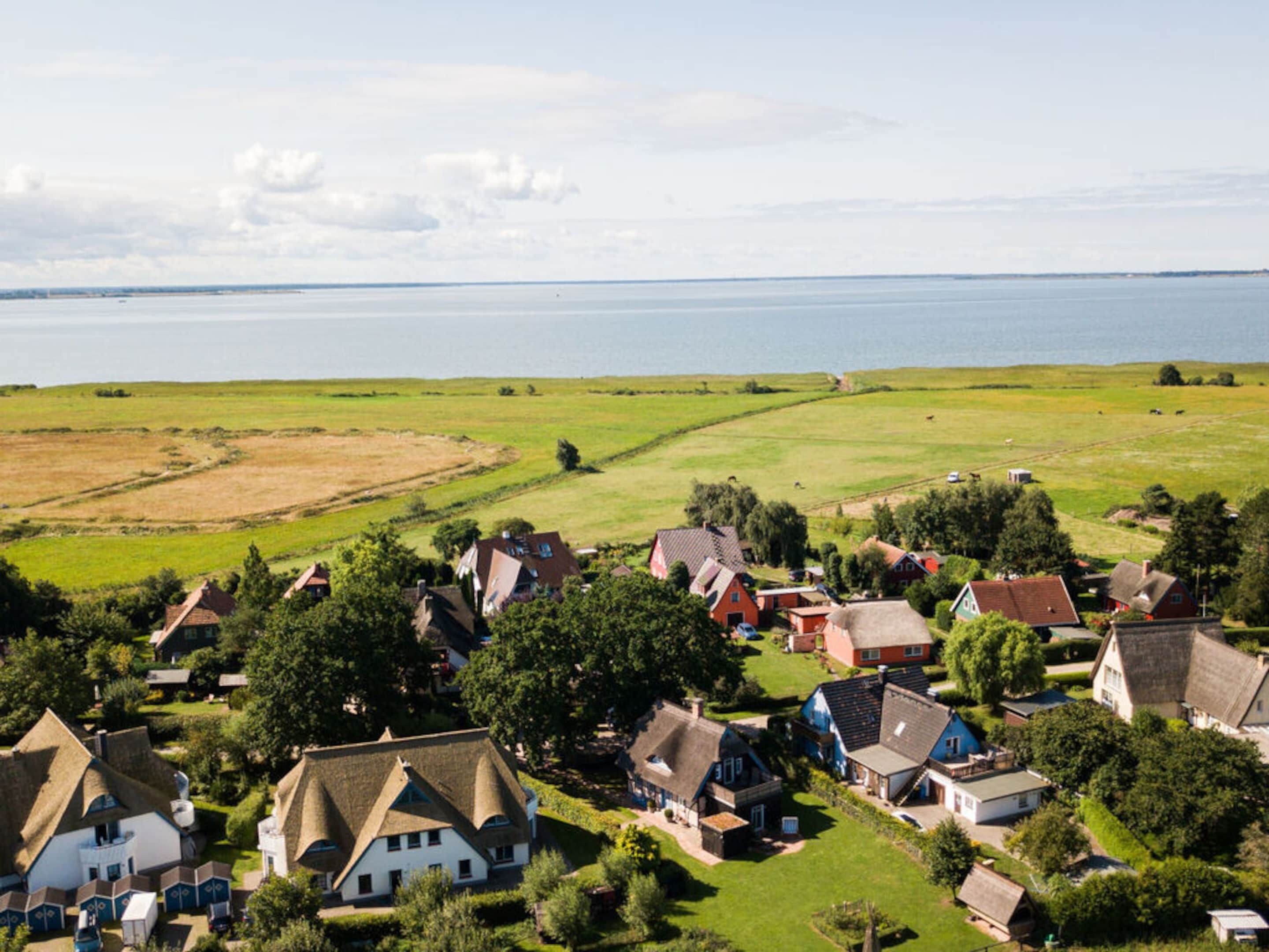 Een kustdorp met traditionele huizen, een uitgestrekte waterpartij en groene velden.