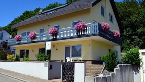 A two-story building with a balcony adorned with pink flowers, a white fence, and a paved driveway. - Palatinate Forest Comfortable Holiday Residence (Silz)