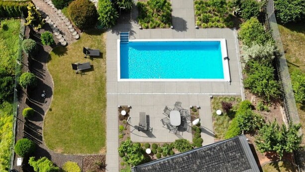An aerial view of a backyard with a rectangular swimming pool, surrounded by a patio area with outdoor furniture and a small garden. - Palatinate Forest Comfortable Holiday Residence (Silz)