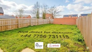 A backyard with a grass area marked with a booking discount code and contact number. - Spacious 5BR Chester | Group & Contractor Stays (Cheshire West and Chester)