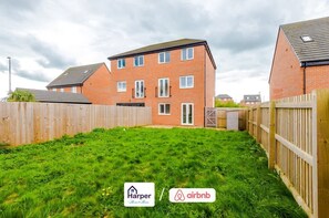 Un appartement aux murs de briques rouges, doté d’une cour arrière clôturée, où l’on peut voir les logos de Harper et d’Airbnb, et un ciel nuageux.