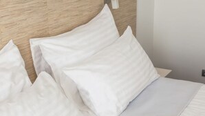 A neatly made bed with white linens and pillows, a wooden headboard, and a plain wall. - Riechey Comfortable Holiday Residence (Fehmarn)
