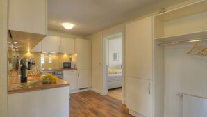 A compact kitchen with white cabinets, a microwave, and a countertop with a bottle and glasses. - Riechey Comfortable Holiday Residence (Fehmarn)