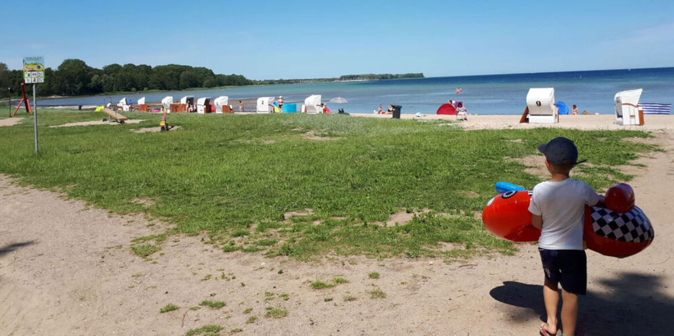 A beach with tents and beach chairs, a grassy area, and a body of water.